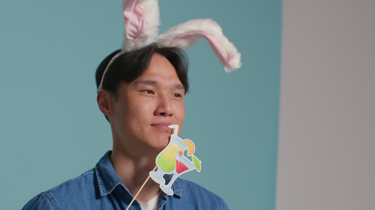 파란색 스튜디오 배경 앞에 있는 남자가 장비로 사진 부스 스타일의 초상화를 위해 재미있게 옷을 입고 포즈를 취하고 있습니다.