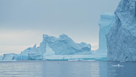 Gran-Puesta-De-Sol-Del-Paisaje-Marino-Del-Iceberg-De-La-Antártida,-Grandes-Icebergs-Azules-Masivos-Con-Formas-Asombrosas-Y-Nubes-Dramáticas-Y-Cielo-En-El-Paisaje-Invernal-Del-Amanecer-En-La-Península-Antártica-En-Una-Escena-Helada