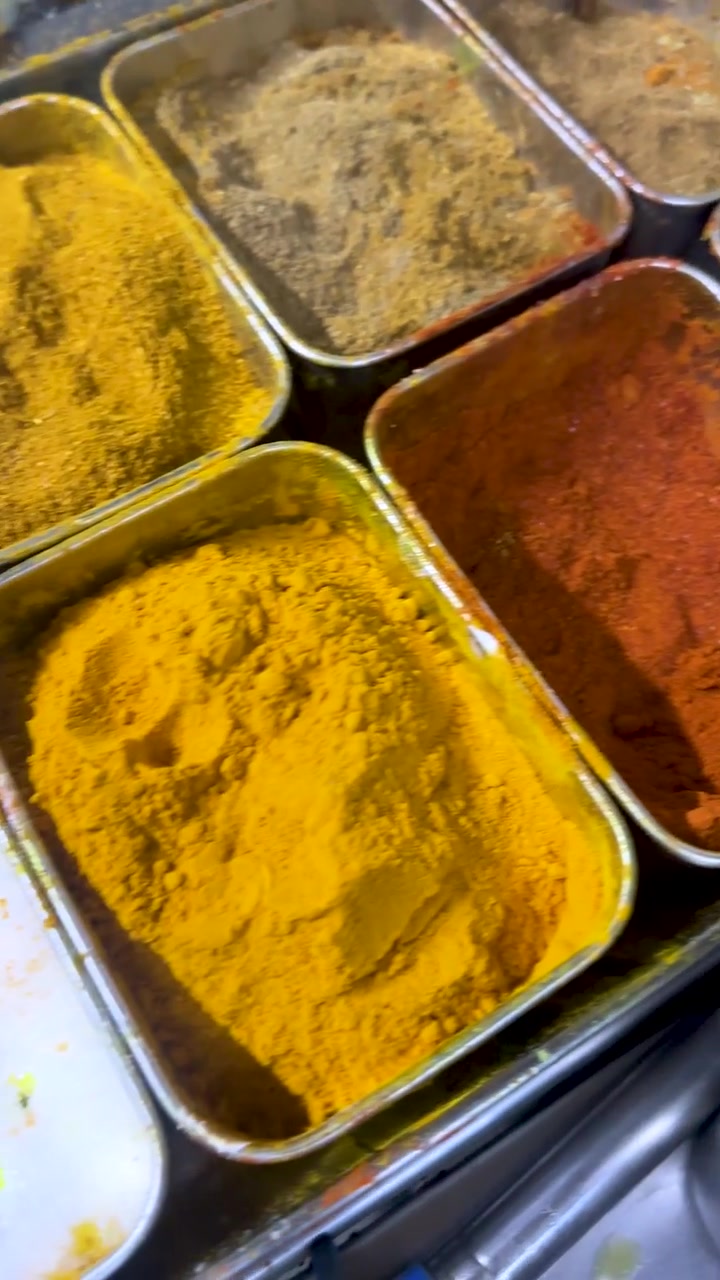 A smooth camera pan reveals vibrant ground spices and salt arranged in stainless steel containers.