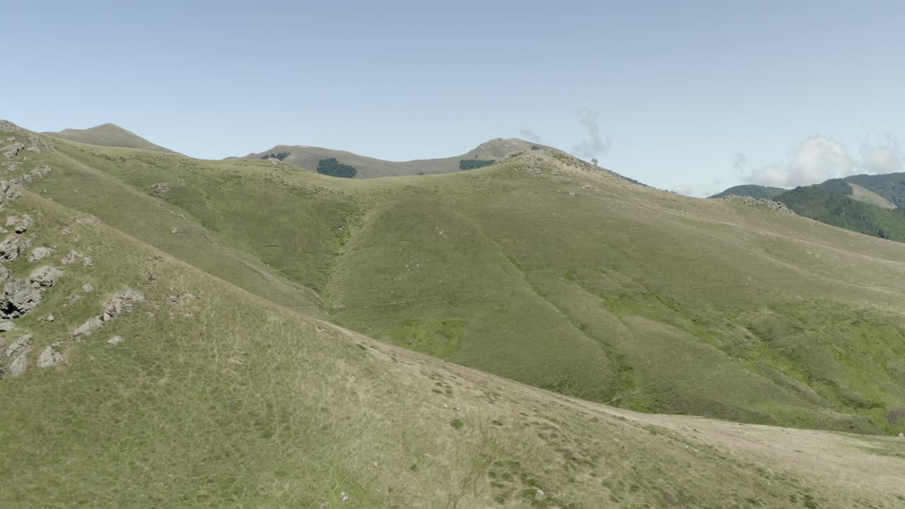 Aerial view flying over sunlit grassy mountain slope, revealing expansive Pyrenees landscape, Col de Sourzay, Lecumberry, France
