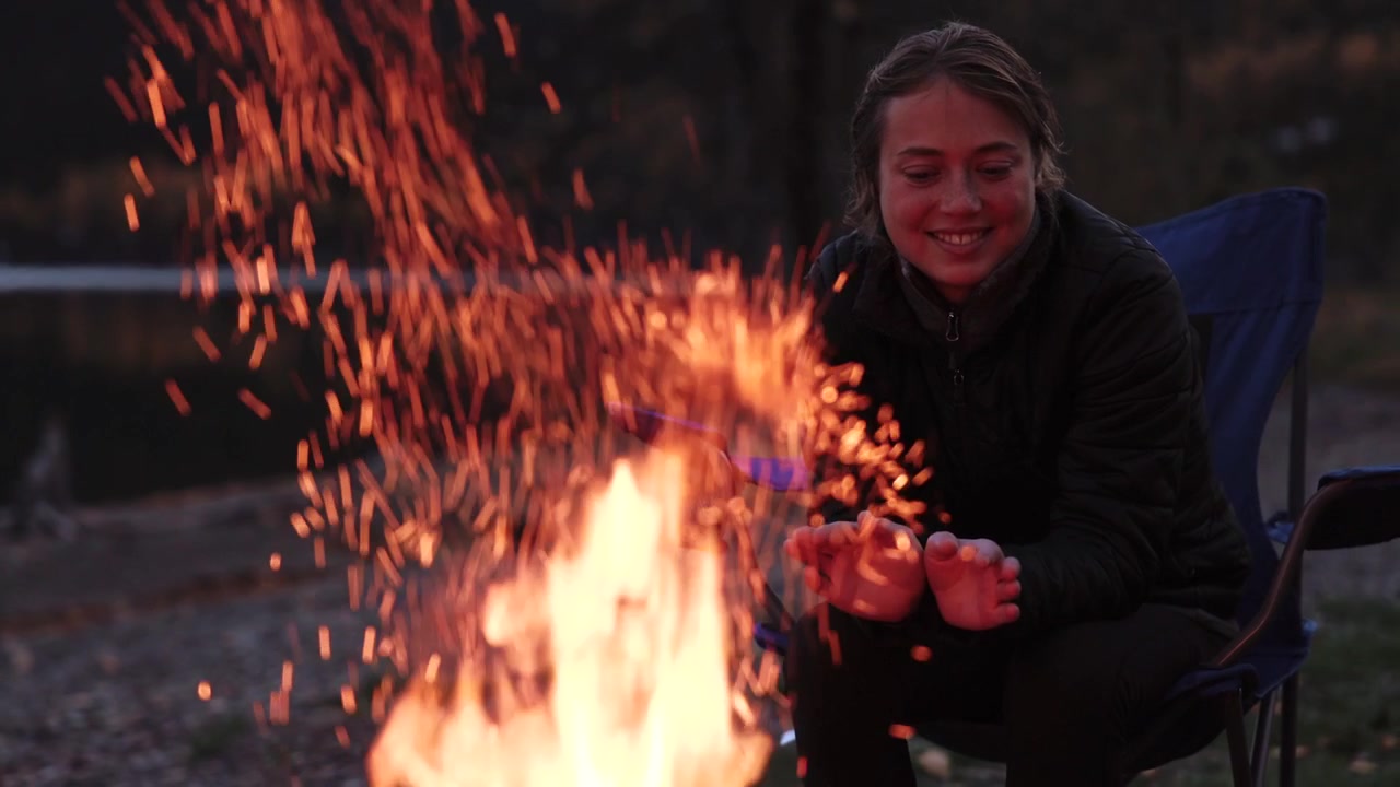 Young Woman Enjoying Campfire By Lake At Dusk