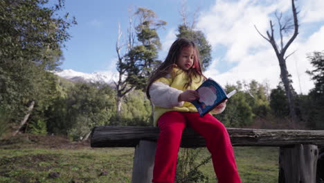 young girl reads a book while sitting on a rustic wooden benchl, surrounded by forest, mountains, and soft morning light in patagonia, argentina, slow motion , camera sliding