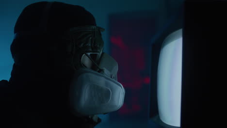 person watching a retro tv in a dark room wearing a gas mask