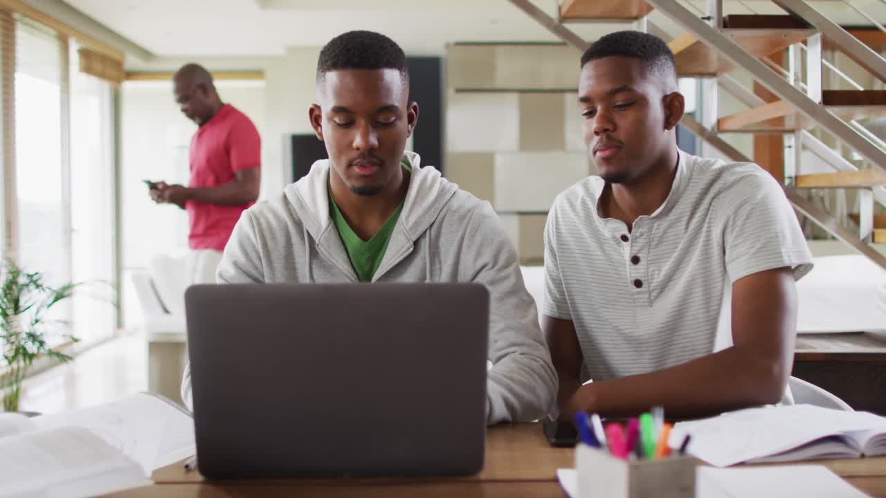 To afrikansk-amerikanske teenagetvillingebrødre bruger en bærbar computer og taler med far i baggrunden.