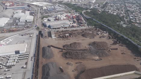 aerial footage showcasing scrap piles, heavy machinery, freight containers, and surrounding industrial infrastructure in a shipyard.