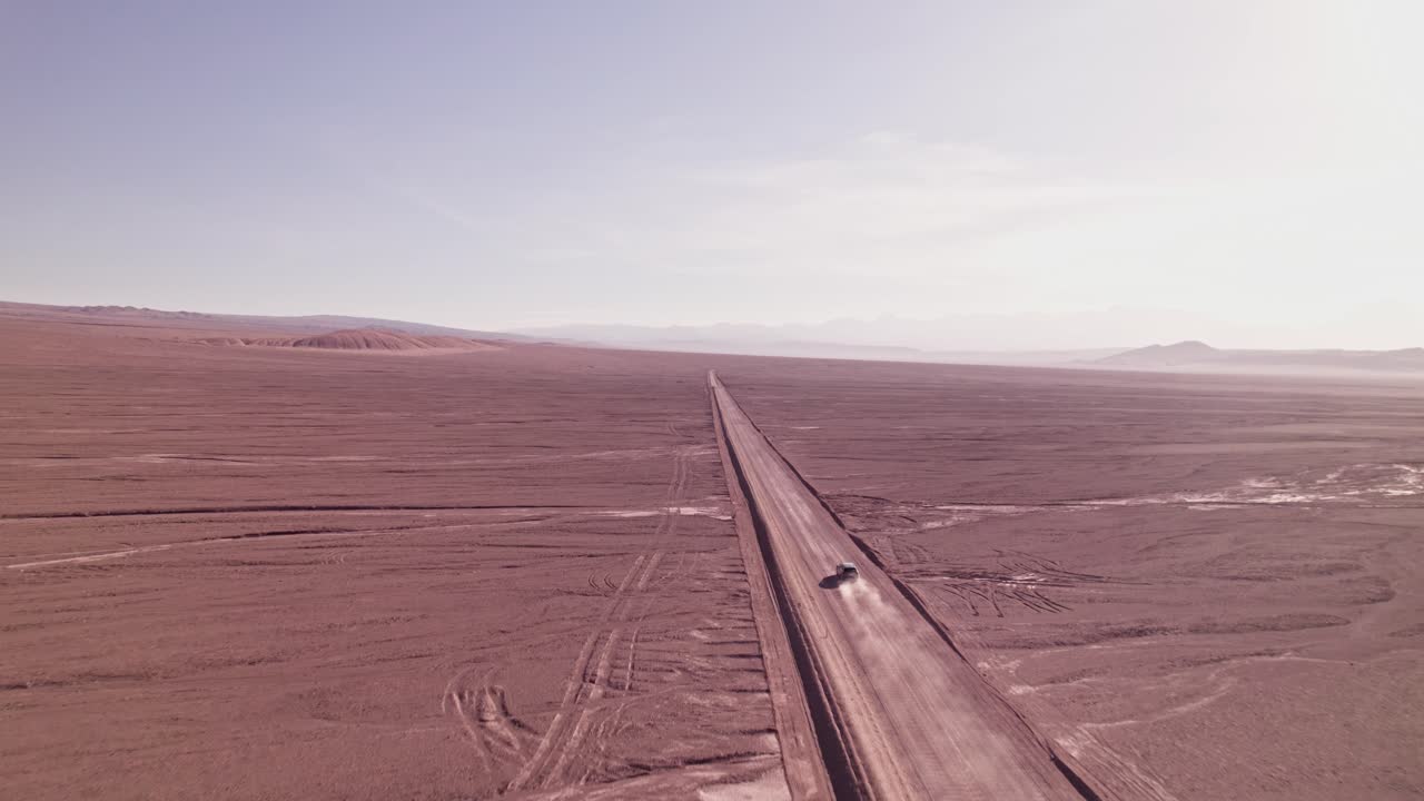 Drone view of an off-road vehicle driving through the vast Atacama Desert, Chile. Dust trails rise behind the car as it speeds across the endless barren landscape under bright sunlight
