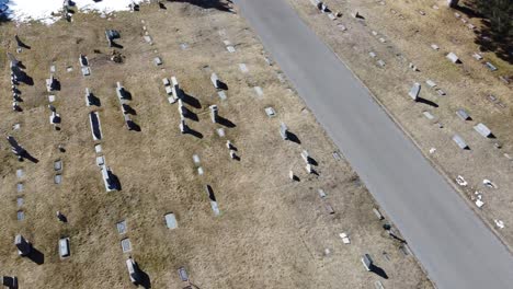 drone looking down at a cemetery with gravestones flying straight a few seconds then panning or whipping to the left before coming to a stop, on a sunny winter day with patches of snow on the ground