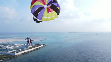 couple on island vacation taking selfie while parasailing over sky blue sea, drone follow