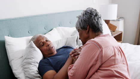 senior woman comforting man with illness lying in bed at home