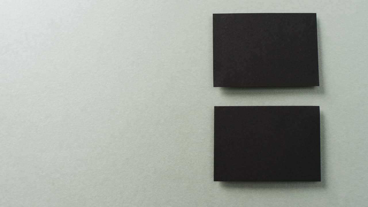 Overhead view of two black business cards arranged on grey background, copy space, slow motion