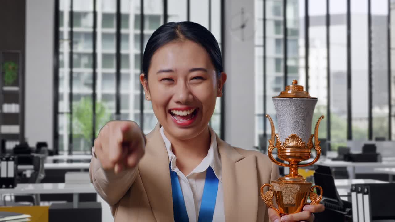 Close Up Of Asian Business Woman In A Suit With A Gold Medal And Trophy Touching Her Chest Then Smiling And Pointing To Camera Being Proud Of Herself In The Office