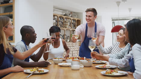 group of men and women making toast as they enjoy eating meal prepared in kitchen cookery class