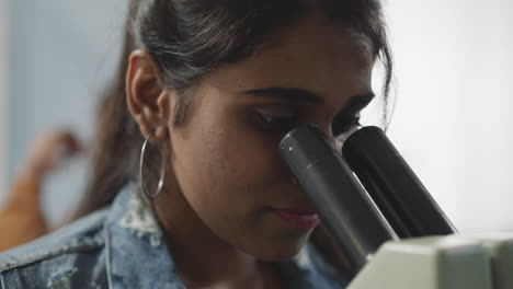 mujer india mira a través del microscopio en un fondo borroso