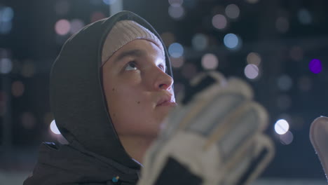 close-up of a focused man wearing gloves gazing upward during a nighttime training session, the blurred background features glowing city lights