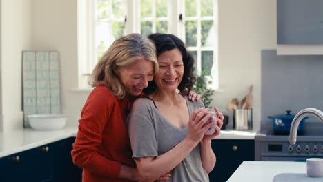 loving same sex mature female couple drinking coffee and hugging in kitchen together