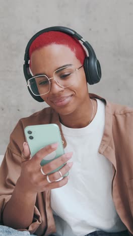 young african american woman listens to music on headphones and holds phone
