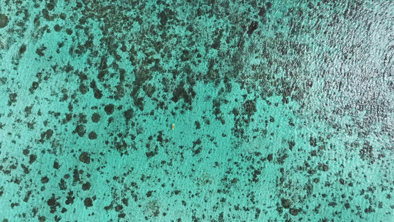 A stunning top-down drone view of a kayak floating on the clear turquoise waters near the Cook Islands