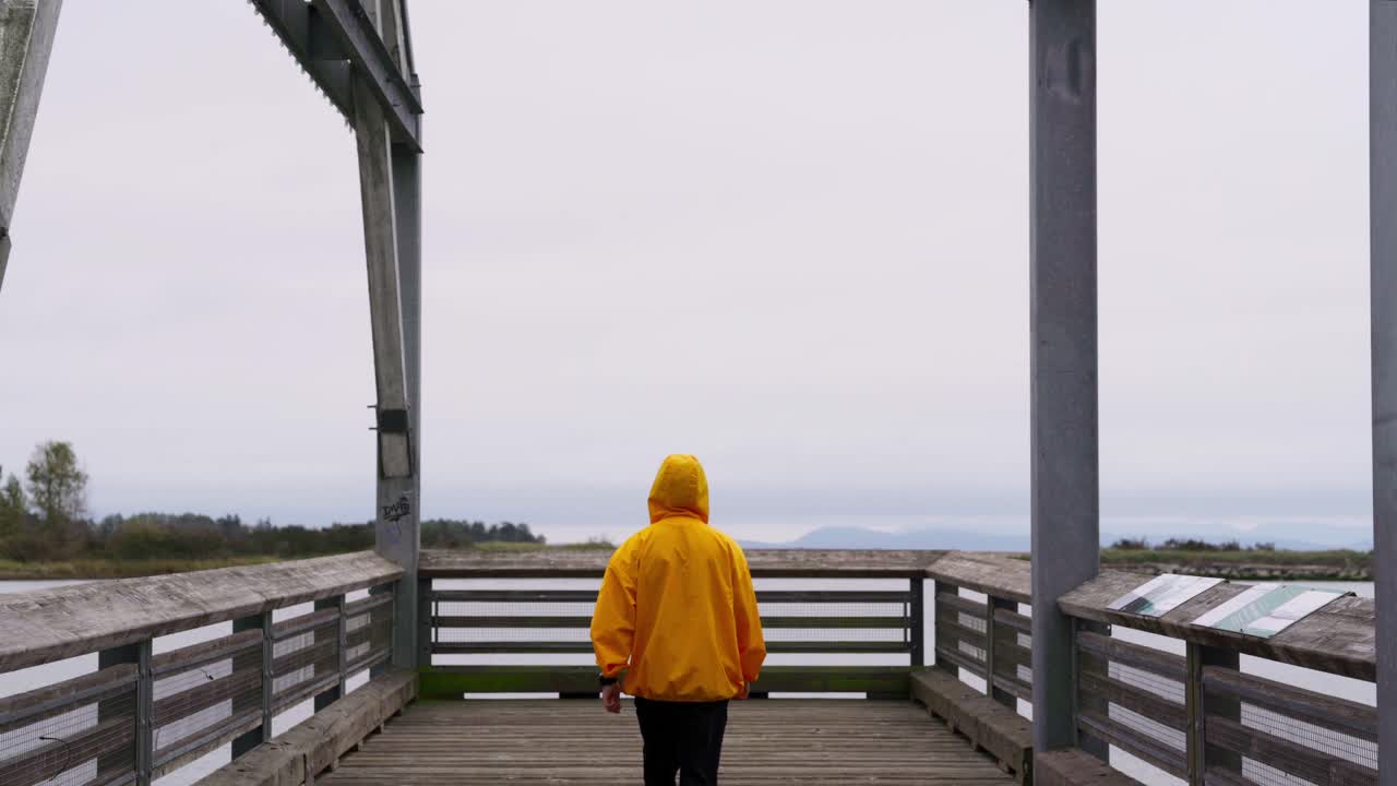 Medium Shot of a person in a yellow jacket walks dockside overlooking a pier of fishing boats
