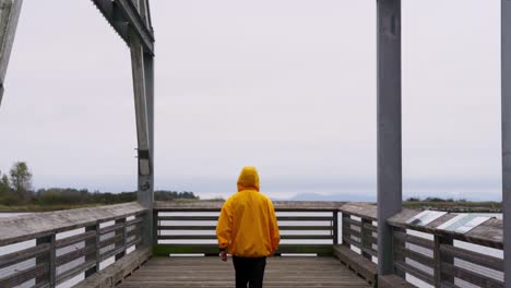 Medium-Shot-of-a-person-in-a-yellow-jacket-walks-dockside-overlooking-a-pier-of-fishing-boats