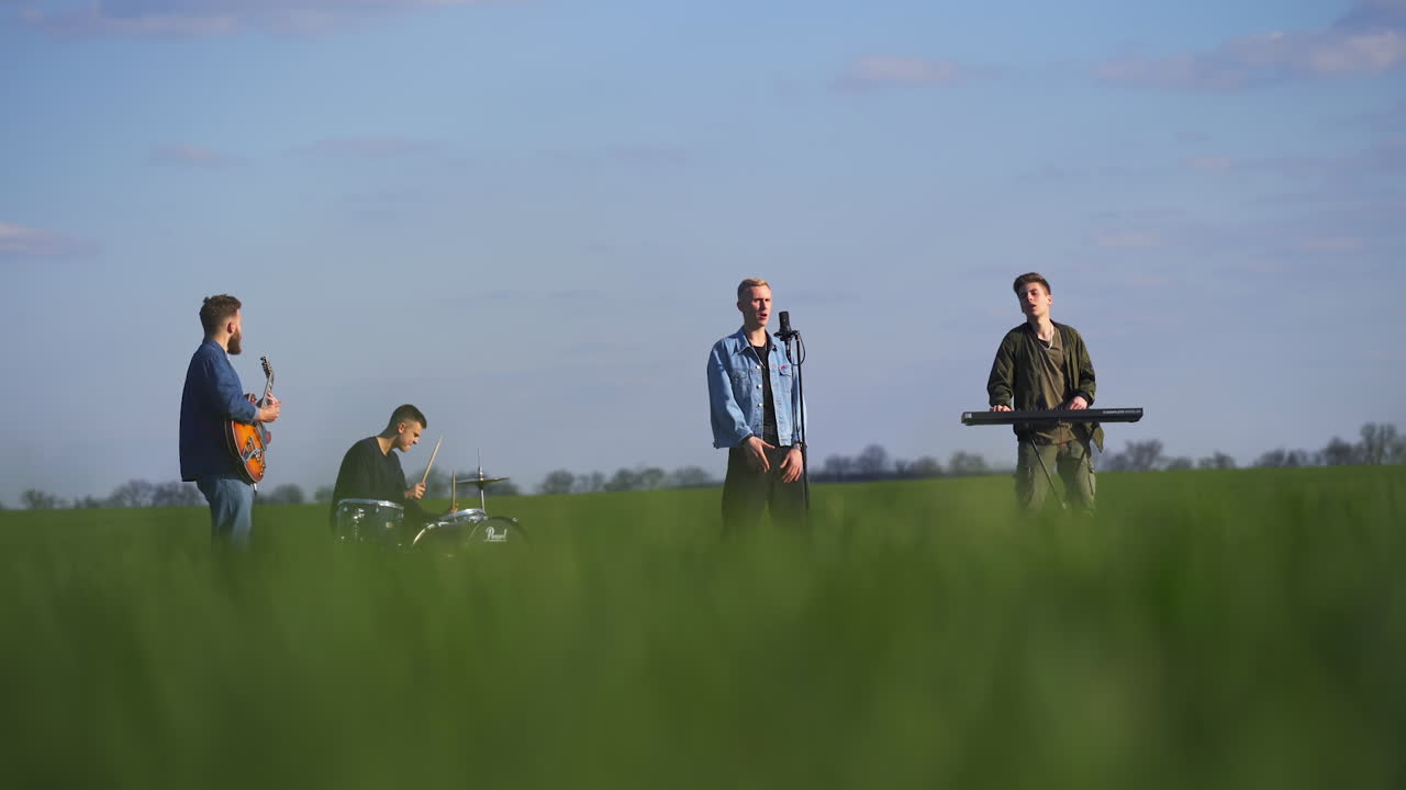 Four men music band sing and play music in the farmlands. Young group making music. Blurred foreground.