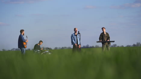 four men music band sing and play music in the farmlands. young group making music. blurred foreground.