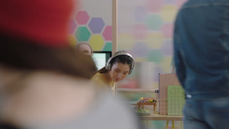 Gente-De-Negocios-Feliz-Reuniéndose-Con-Una-Mujer-Líder-Del-Equipo-Caucásico-Mostrando-Ideas-De-Estudiantes-Asiáticos-Apuntando-Al-Soporte-Para-Compartir-Pantalla-Discutiendo-Un-Proyecto-Creativo-Usando-Tecnología-Informática-En-Una-Oficina-Colorida