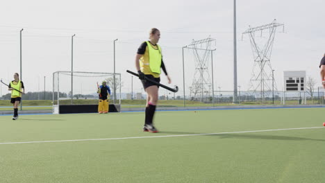 female hockey players practicing on field, focusing on teamwork and strategy