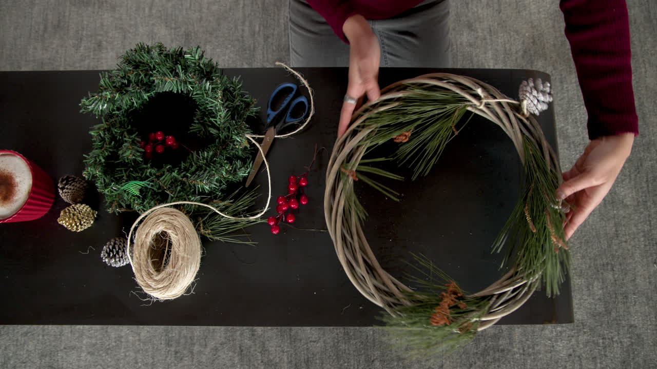 Crafting Christmas wreaths at home, hands decorating with berries and pinecones, copy space