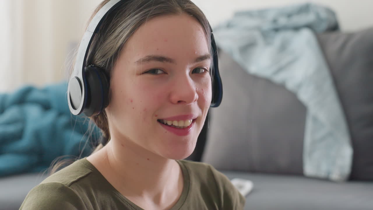 Happy young girl with headphones moving to rhythm of music, eyes closed enjoying melody, relaxed posture reflecting joy and energy, warm indoor lighting