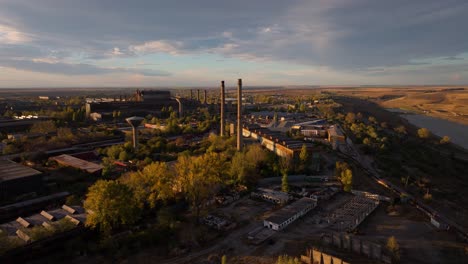 aerial tracking shot over a time-worn industrial area and the towering smokestacks, sunset warm light, 4k50fps