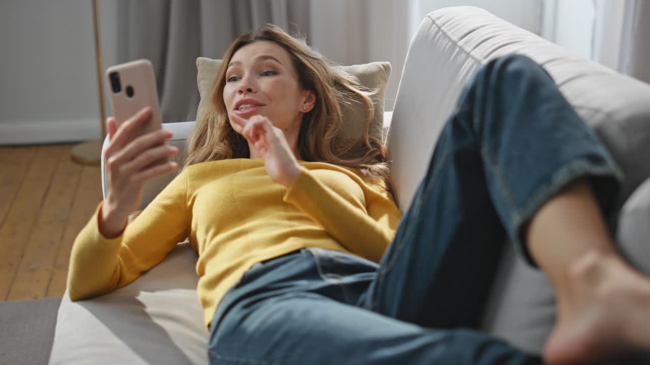 Laughing lady speaking smartphone gesturing hand at home. Relaxed woman laying