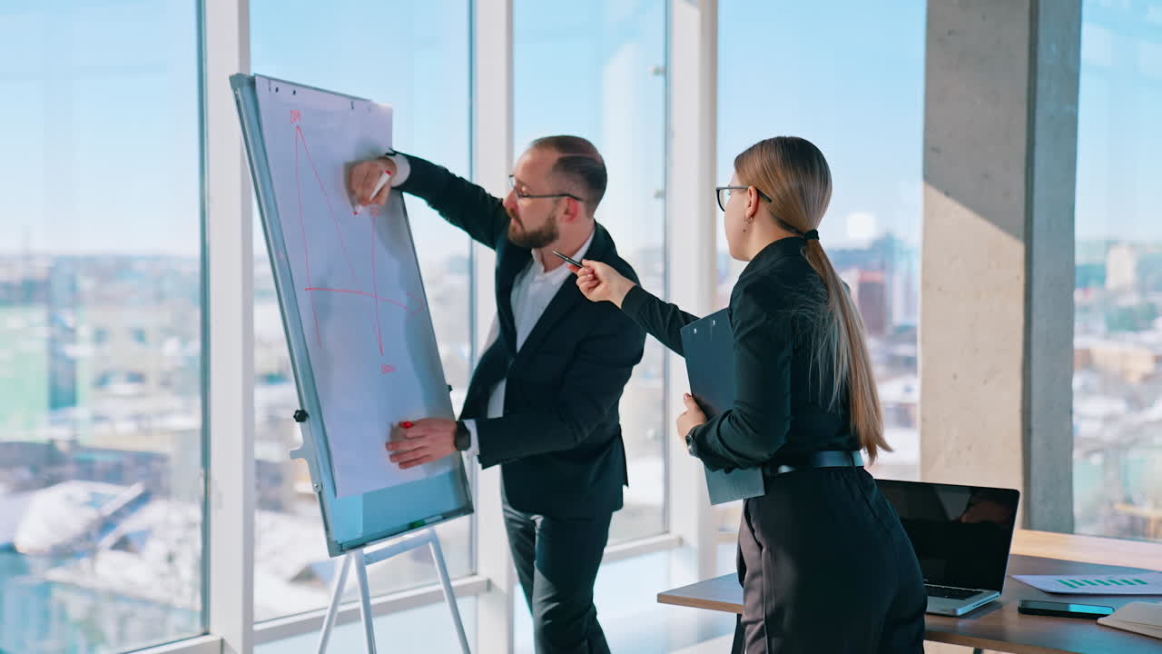 Business coworkers making about new blueprint. Successful man and smart woman in black suits working in office together. Panoramic windows background.