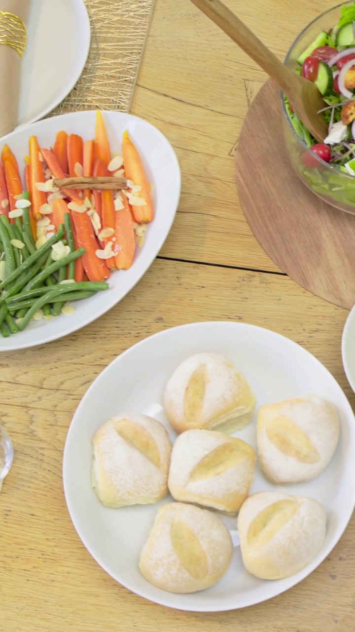 Vídeo vertical: Câmera deslizando revelando uma mesa de refeição em casa com salada e pães em destaque.