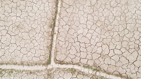 dry cracked drought fractured agricultural land sections aerial view rotating descent above barren damaged landscape