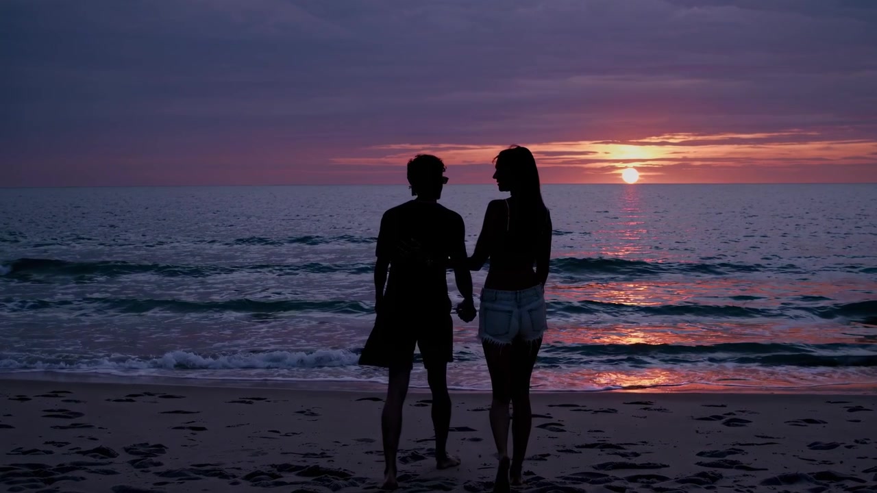 Young Couple Walking Hand in Hand on Beach at Sunset