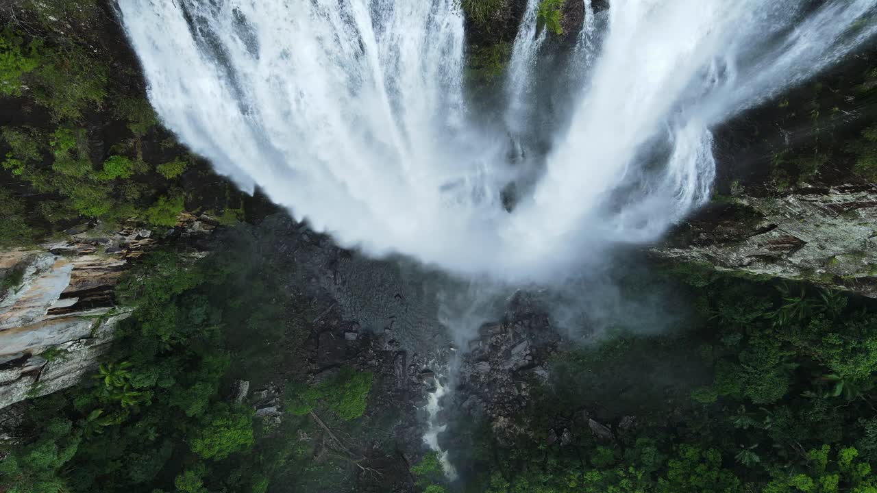 elevándose lentamente sobre una cascada mientras el agua cae con fuerza hacia un exuberante estanque de rocas tropicales debajo
