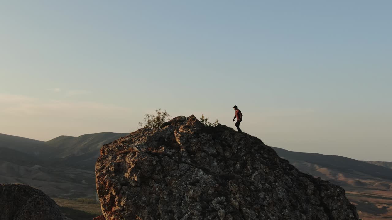 un hombre conquista una roca al atardecer por un estudio aéreo de un avión no tripulado que vuela alrededor de la roca en un círculo en la corteza se encuentra un hombre contra el telón de fondo de la puesta de sol y la montaña panorama de la noche