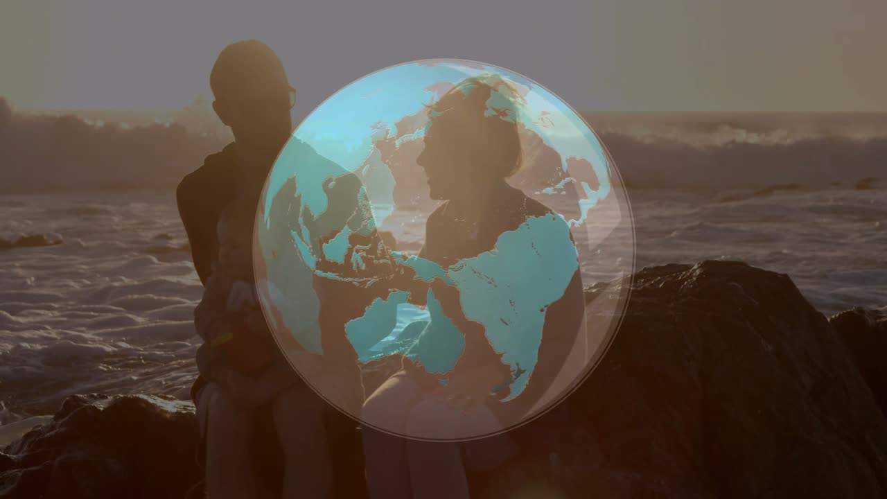 Couple holding baby on rock at sunset globe overlay rotating over ocean obscuring them for travel