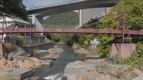 aerial shot flying under bridge above river in jozankei famous onsen town hokkaido, japan