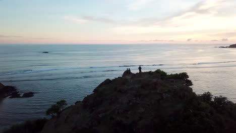 aerial 4k silhouettes standing on edge of cliff near ocean at sunset