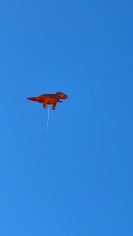 orange dinosaur balloon floating in a clear blue sky