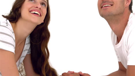 una pareja feliz acostada cara a cara en el suelo, tomados de la mano y mirando hacia arriba.
