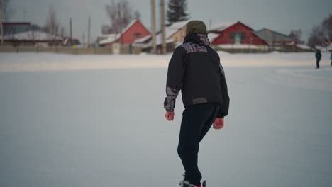young boy skating skillfully among other skater gliding on snowy ice rink with urban buildings in background under pale winter light capturing motion and seasonal leisure atmosphere
