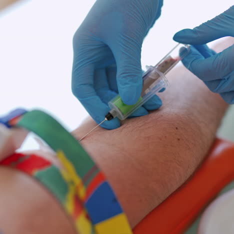 close-up of the process of taking blood from the vein. lab technician pricking needle syringe in the arm patient drawing blood sample for blood test.