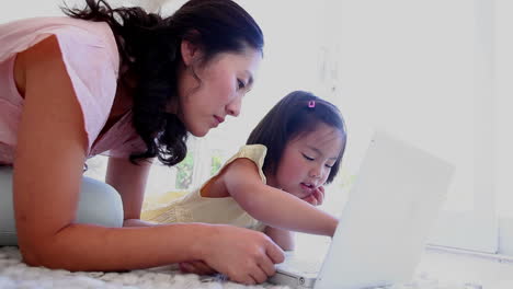 mother and daughter lying together while using a laptop