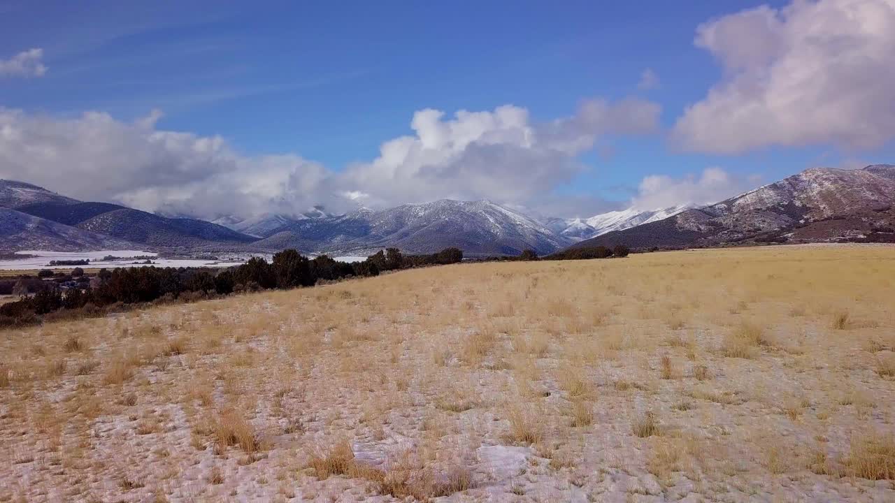 vista aérea del paisaje de pastos con montañas cubiertas de nieve, nubes y cielo azul en la distancia - dolly adelante