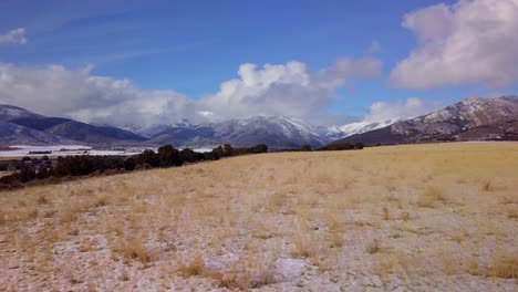 aerial view of pasture landscape with snow-covered mountains, clouds and blue sky in the distance - dolly forward