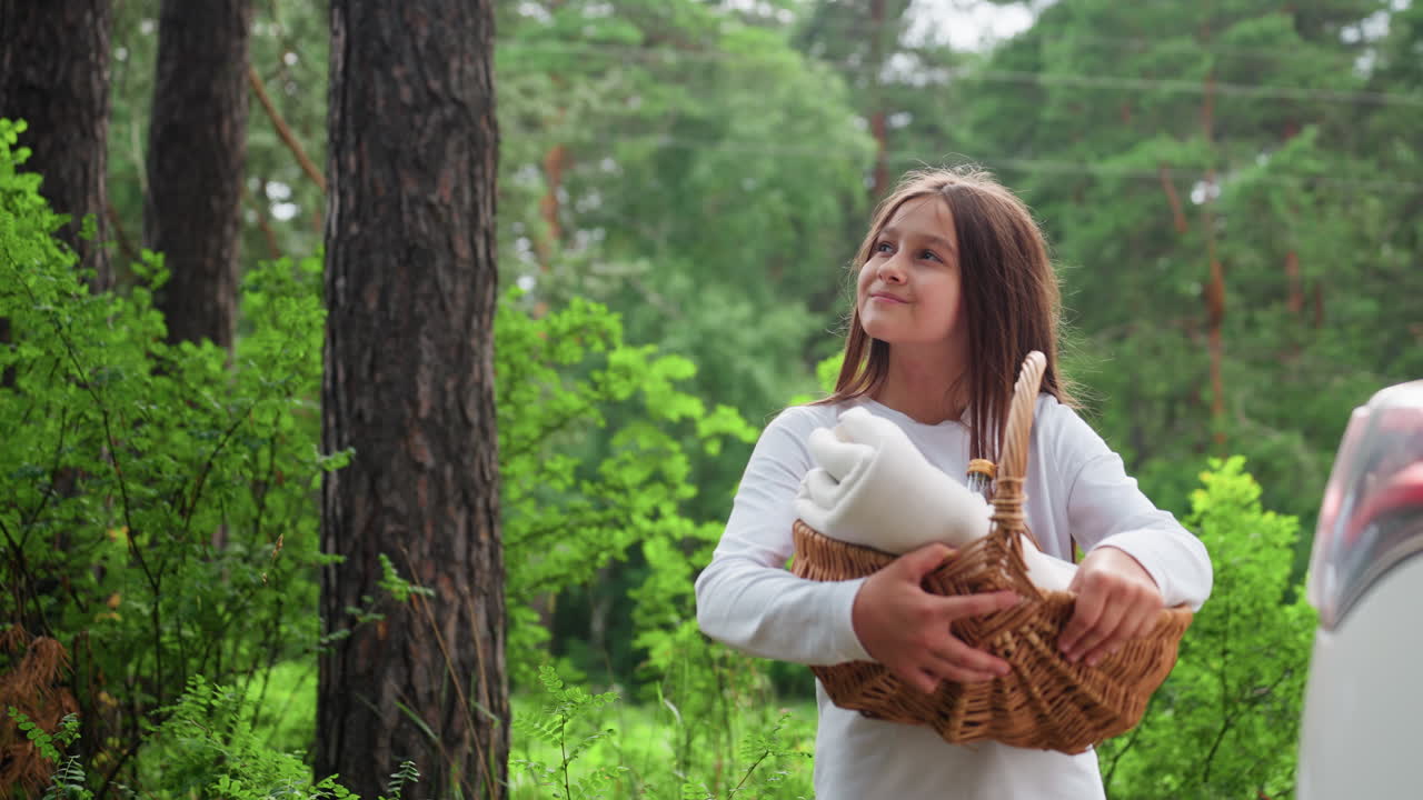 Приблизьте жизнерадостную молодую девушку с корзиной для пикника, радостно улыбающуюся среди пышных зеленых деревьев, наслаждающуюся спокойной природой и свежим воздухом в расслабляющий летний день