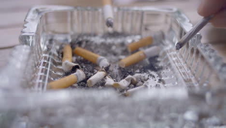 a video captures cigarettes and ashes resting in an ashtray, while a man's hand reaches for a cigarette, preparing to indulge in his nicotine fix