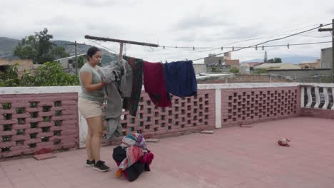 Neighborhood-landscape-in-poor-Latin-American-city,-adult-Latin-woman-working-on-household-chores